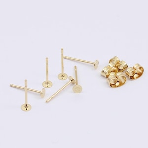 May include: A set of gold earring posts and backs. The posts are straight and have a small round disc at the end. The backs are round and have a small hole in the center.