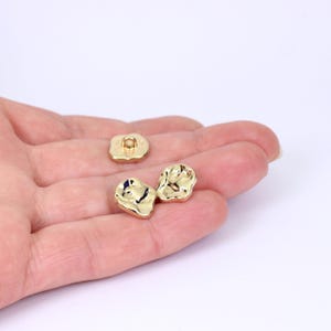 May include: Three gold-coloured buttons with an irregular, textured surface. The buttons have a hole in the centre for sewing.