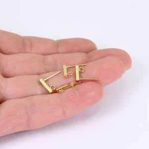 May include: A collection of gold-coloured bar-shaped earring posts with small loops and posts. The earrings are presented against a light background. These earrings are likely for jewellery making or crafting.