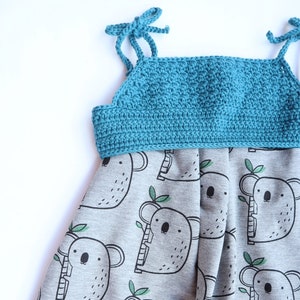 Puede incluir: Un vestido gris sin mangas con un corpiño de crochet turquesa y un patrón de koalas negros sobre un fondo gris.