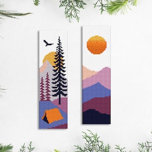 May include: Two cross-stitch bookmark patterns featuring a mountain landscape with a tent, a pine tree, and a sun. The first bookmark features a tent in the foreground, a pine tree, and a sun setting behind the mountains. The second bookmark features a sun setting behind the mountains.