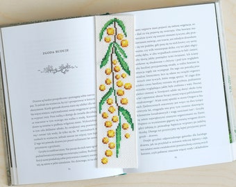 May include: A close-up of a book with a bookmark featuring a green and yellow embroidered floral design. The text on the page reads "Zgoda Buduje".