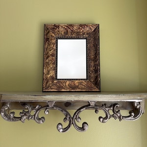 Puede incluir: Una taza de cerámica blanca con un asa negra y el texto "But First, Coffee" en negrita negra. La taza se encuentra sobre un fondo borroso, sugiriendo un ambiente acogedor.