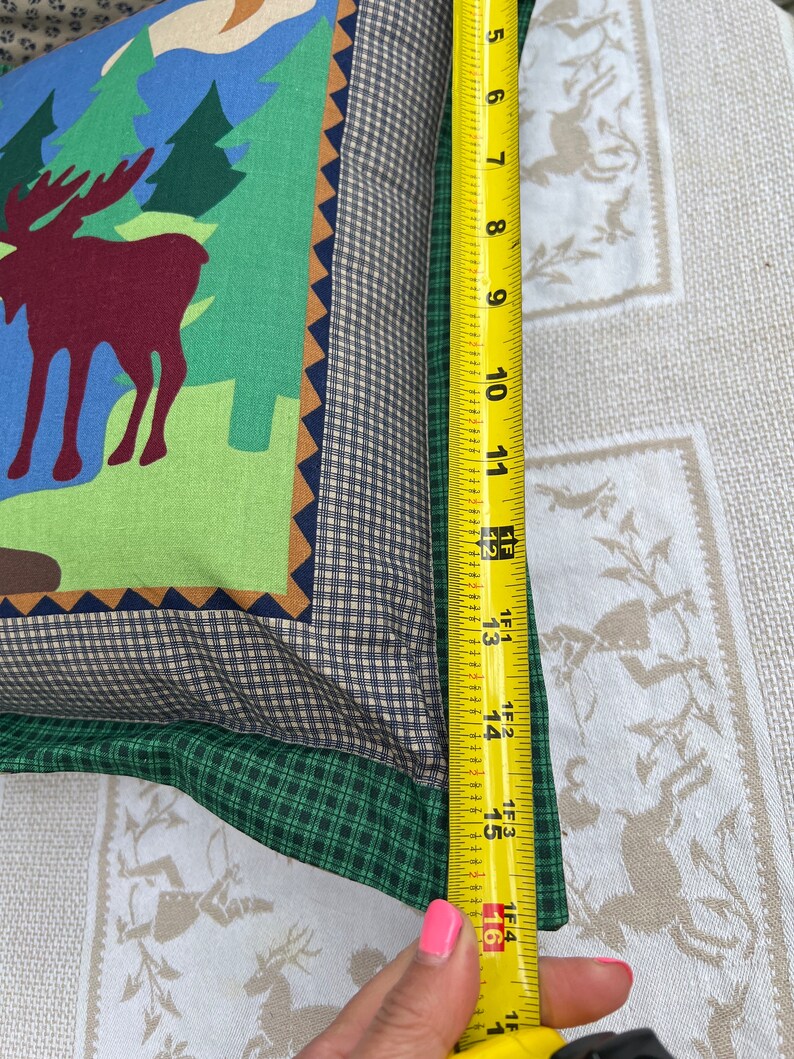 May include: A green, brown, and blue pillow with a moose design. The pillow is 16 inches long.