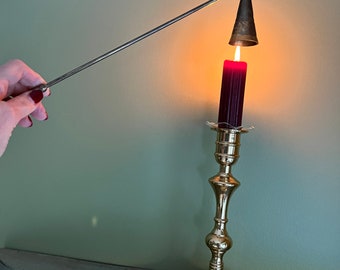 May include: A brass candlestick with a red candle lit by a metal candle lighter. The candle lighter is held by a hand with red nail polish.