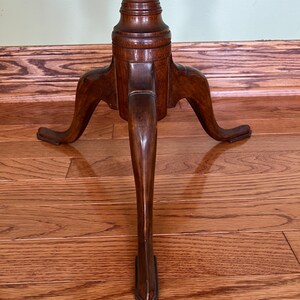 May include: A wooden tripod table with a turned pedestal and three legs. The legs are tapered and end in a pointed tip. The table is made of dark wood and has a smooth finish.