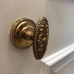 Könnte beinhalten: Ein goldener Türknauf mit einem verzierten Design. Der Knauf ist oval geformt und hat ein erhabenes Blumenmuster.