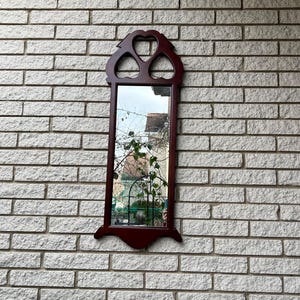May include: A mahogany wood framed mirror with a heart-shaped design. The mirror is rectangular and has a beveled edge.