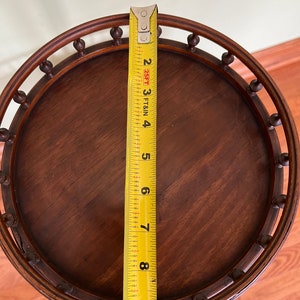 May include: A round wooden table top with a decorative edge and a yellow measuring tape next to it. The table top is 9 inches in diameter.