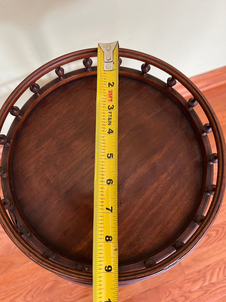 May include: A round wooden table top with a decorative edge and a yellow measuring tape next to it. The table top is 9 inches in diameter.