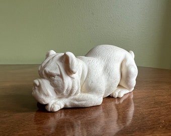 Può includere: Scultura in ceramica bianca di un bulldog sdraiato con la testa appoggiata sulle zampe.