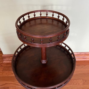 May include: A two-tiered mahogany serving table with a round top and a decorative, scalloped edge. The table has a turned pedestal and three cabriole legs.
