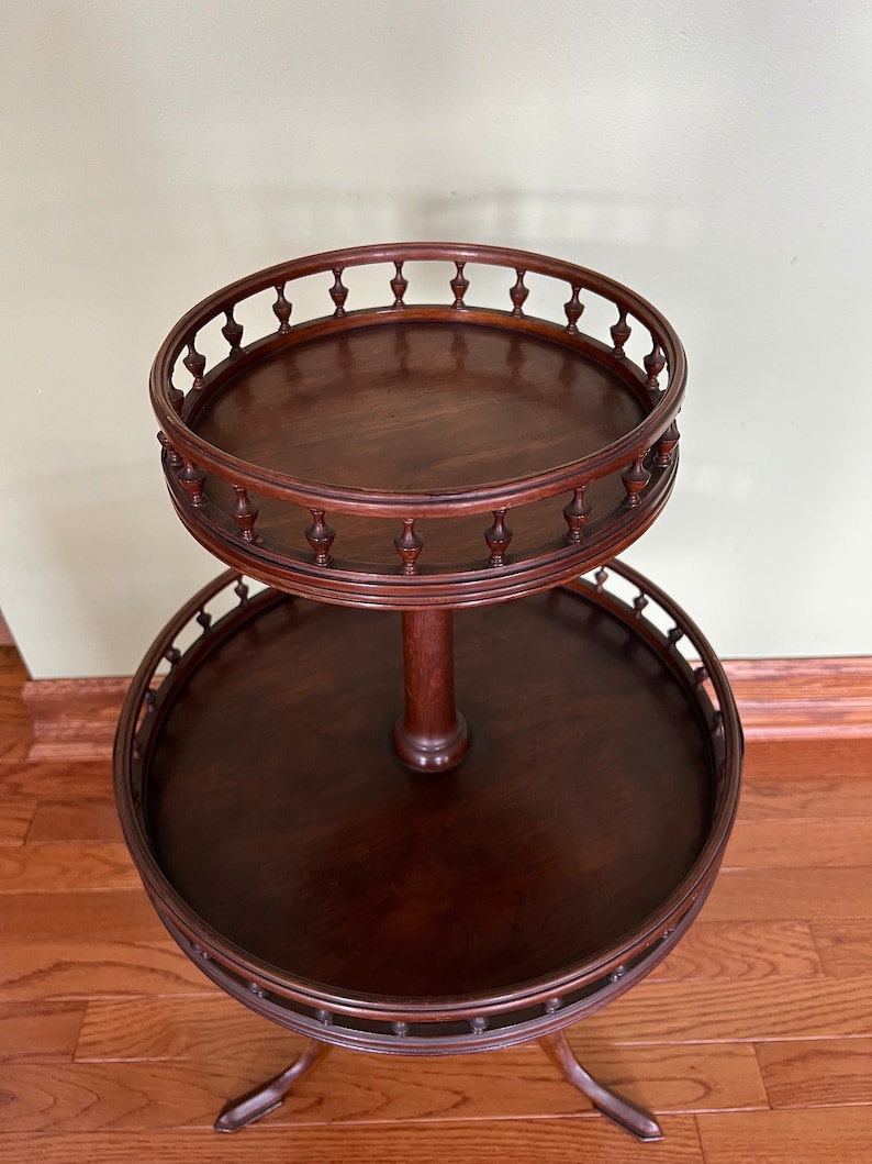 May include: A two-tiered mahogany serving table with a round top and a decorative, scalloped edge. The table has a turned pedestal and three cabriole legs.