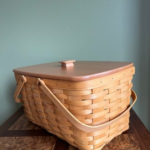 Puede incluir: Una cesta tejida natural con una tapa y asas de madera. La cesta est&aacute; hecha de mimbre marr&oacute;n claro y tiene una forma rectangular.