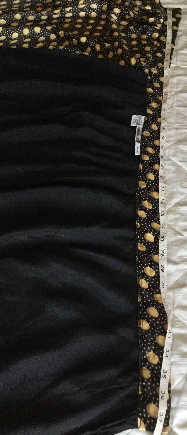 May include: Black dress with a polka dot pattern on the top and trim. The dress is measured with a tape measure, showing a length of approximately 37 inches. The brand tag reads "ANNE KLEIN".