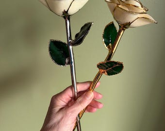 May include: Two decorative roses with cream-colored petals and green leaves. One rose has a silver stem, the other a gold stem. The petals are outlined in a contrasting color, adding detail to the floral design.