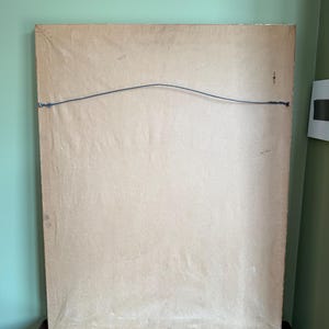 May include: The back of a rectangular picture frame featuring a light brown paper backing. A thin, dark metal hanging wire is attached to the frame with small metal fasteners on each side, creating a curved line across the upper portion.