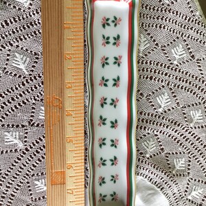 May include: A white porcelain trinket dish with a green and red border and a repeating pattern of red and green holly leaves. The dish is approximately 6 inches long.