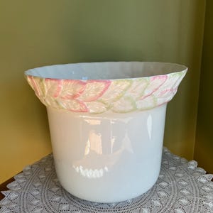 May include: White ceramic planter with a raised floral design around the rim. The flowers are pink and green.