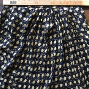 May include: A navy blue skirt with a repeating pattern of large, off-white polka dots. The skirt is pleated at the waist. A wooden ruler is placed across the top of the skirt.