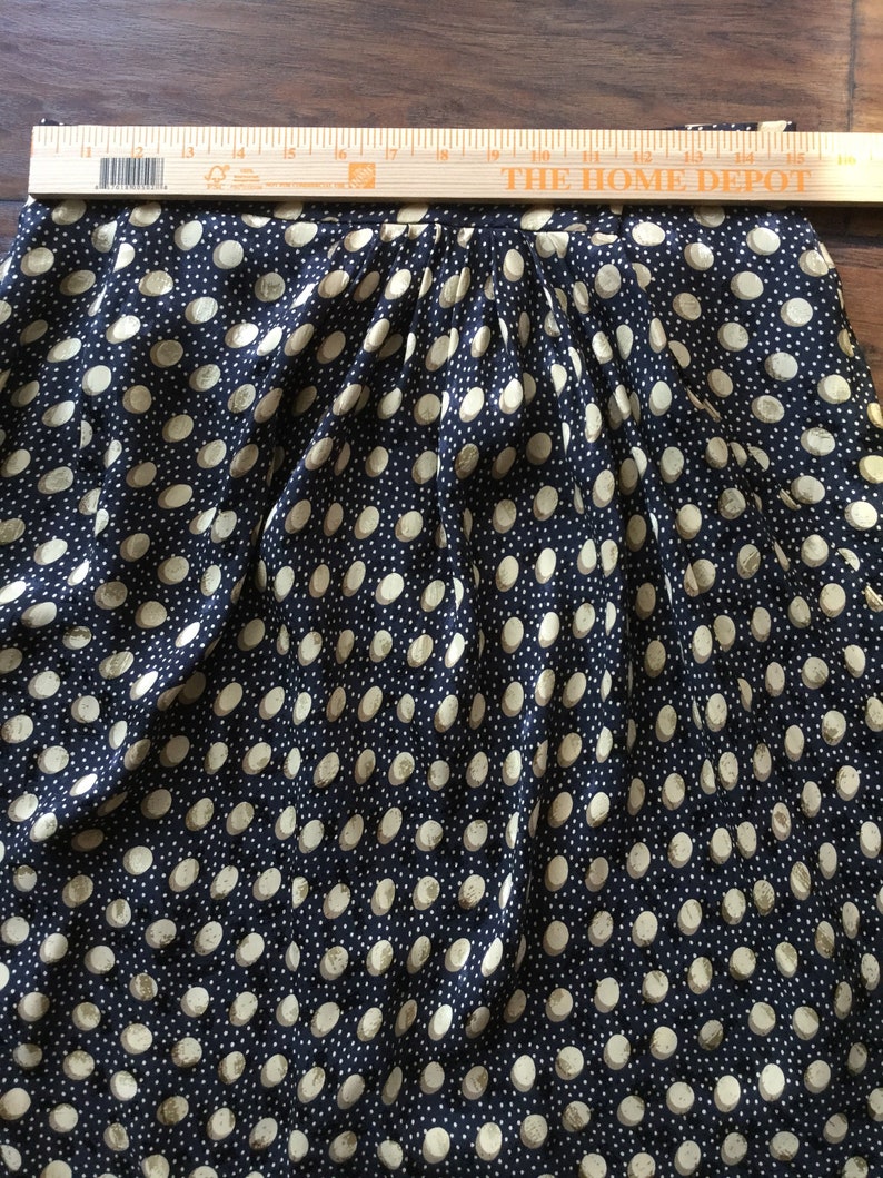 May include: A navy blue skirt with a repeating pattern of large, off-white polka dots. The skirt is pleated at the waist. A wooden ruler is placed across the top of the skirt.