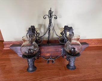May include: A rustic wall sconce with four glass globe candle holders. The sconce features a dark wood base, ornate wrought iron accents, and a decorative chain. The candle holders are supported by decorative metal posts.