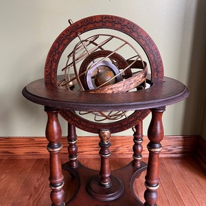 May include: A wooden globe stand with a brass globe and a decorative wooden base. The globe is surrounded by a brass ring with the words "ZONA TEMP MERID. ZONA FREDDA MERID. ZONA TEMP MERID. ZONA TORRIDA" inscribed on it.