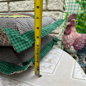 May include: Two green, brown, and white patterned throw pillows with a yellow measuring tape next to them. The tape measure reads 9 inches.