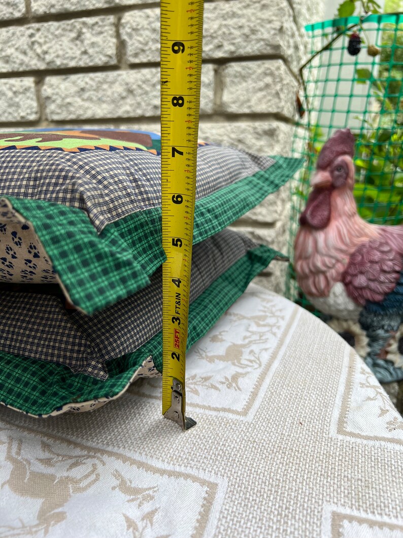 May include: Two green, brown, and white patterned throw pillows with a yellow measuring tape next to them. The tape measure reads 9 inches.