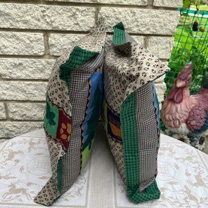 May include: Two decorative throw pillows with a patchwork design featuring green, brown, blue, and beige fabric. The pillows have a green and white plaid trim.