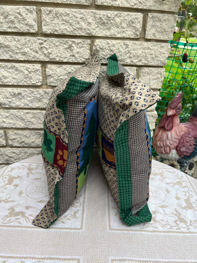 May include: Two decorative throw pillows with a patchwork design featuring green, brown, blue, and beige fabric. The pillows have a green and white plaid trim.