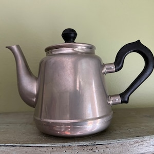 May include: A silver teapot with a black handle and knob. The teapot has a shiny, metallic finish.
