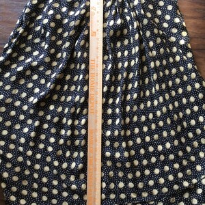 May include: A navy blue skirt with a repeating pattern of beige polka dots. The skirt is pleated and has a length of approximately 20 inches, as measured with a wooden ruler.