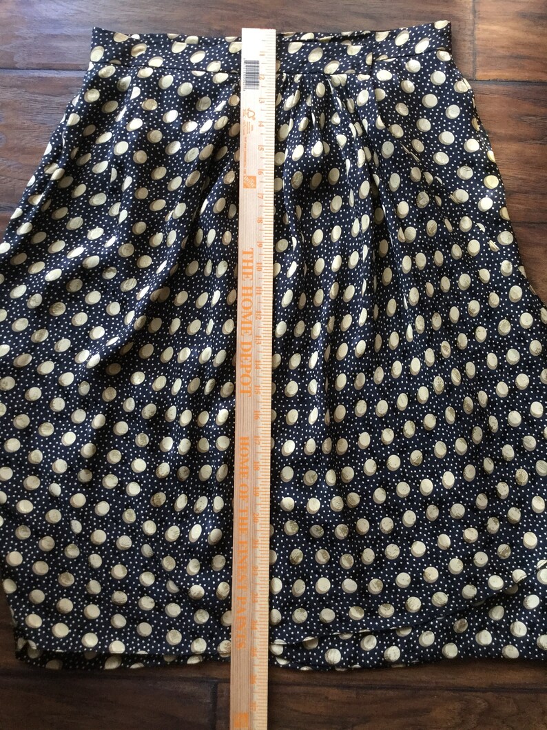 May include: A navy blue skirt with a repeating pattern of beige polka dots. The skirt is pleated and has a length of approximately 20 inches, as measured with a wooden ruler.