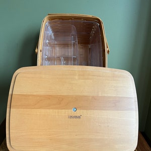 Puede incluir: Una bandeja de servir de madera Longaberger con una cesta de pl&aacute;stico transparente en su interior. La bandeja tiene un acabado de madera clara y el logotipo de Longaberger es visible en la parte inferior.