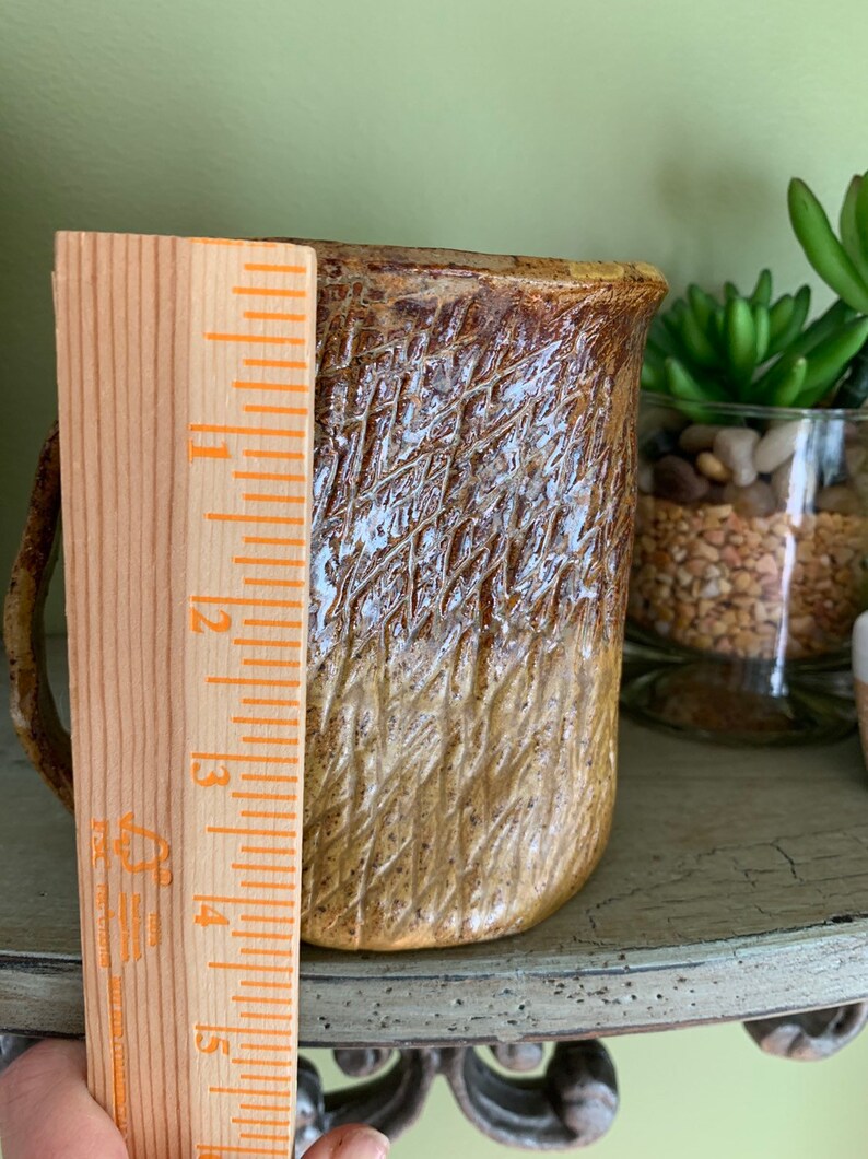 May include: A brown and white ceramic mug with a textured surface. The mug is approximately 5 inches tall.
