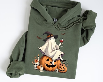May include: A green hoodie with a graphic of a ghost wearing a witch's hat and holding a glass of wine. The ghost is sitting on a jack-o'-lantern.