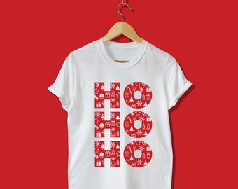 May include: White t-shirt with the word "HO HO HO" in red, Christmas-themed patterns. The letters are filled with festive icons like snowflakes, gifts, and Christmas trees. The shirt is hanging on a wooden hanger against a red background.