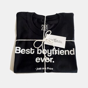 May include: A black t-shirt with white text that reads "Best boyfriend ever. - just ask Pupa". The shirt is folded and tied with twine.