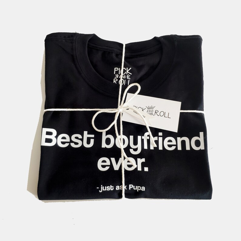 May include: A black t-shirt with white text that reads "Best boyfriend ever. - just ask Pupa". The shirt is folded and tied with twine.