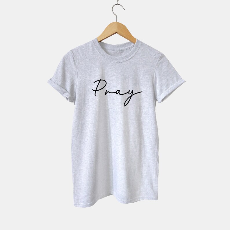 May include: A heather grey t-shirt with the word "Pray" written in black cursive script.