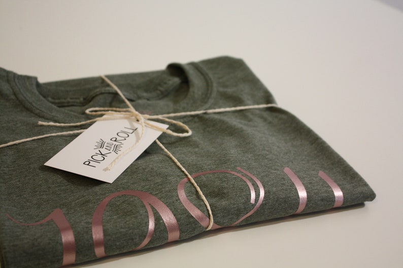 May include: A folded green t-shirt with a rose gold "You" design. The shirt is tied with twine and has a white tag that reads "Pick and Roll".