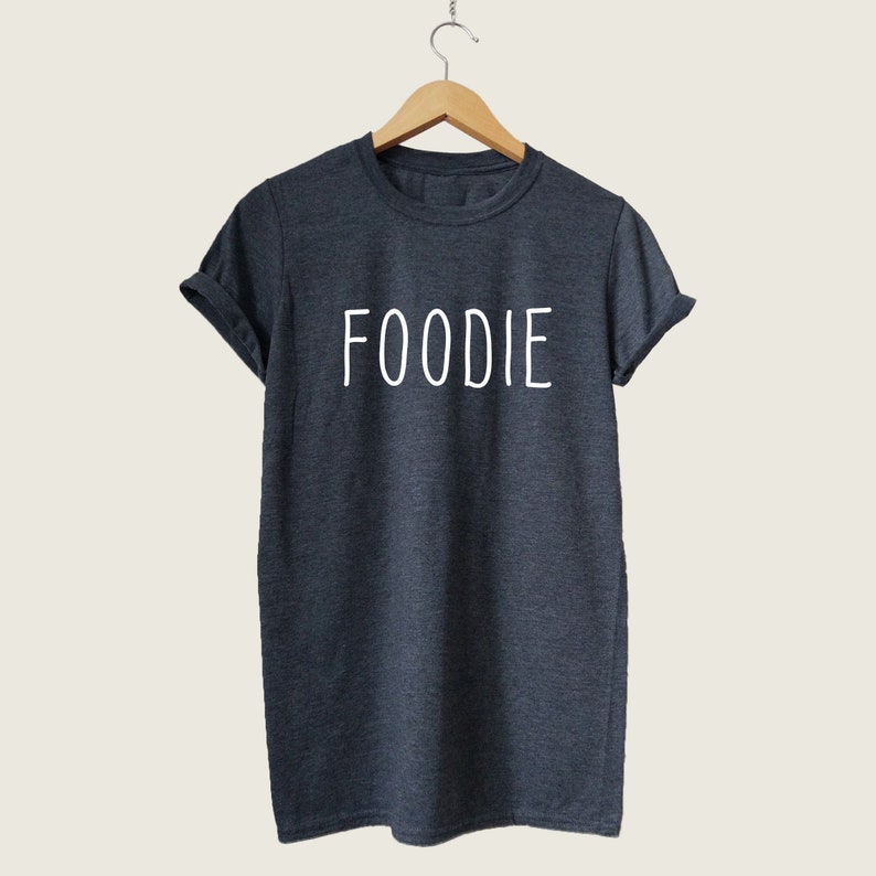 Puede incluir: Una camiseta gris oscuro con la palabra "FOODIE" impresa en blanco en la parte delantera.