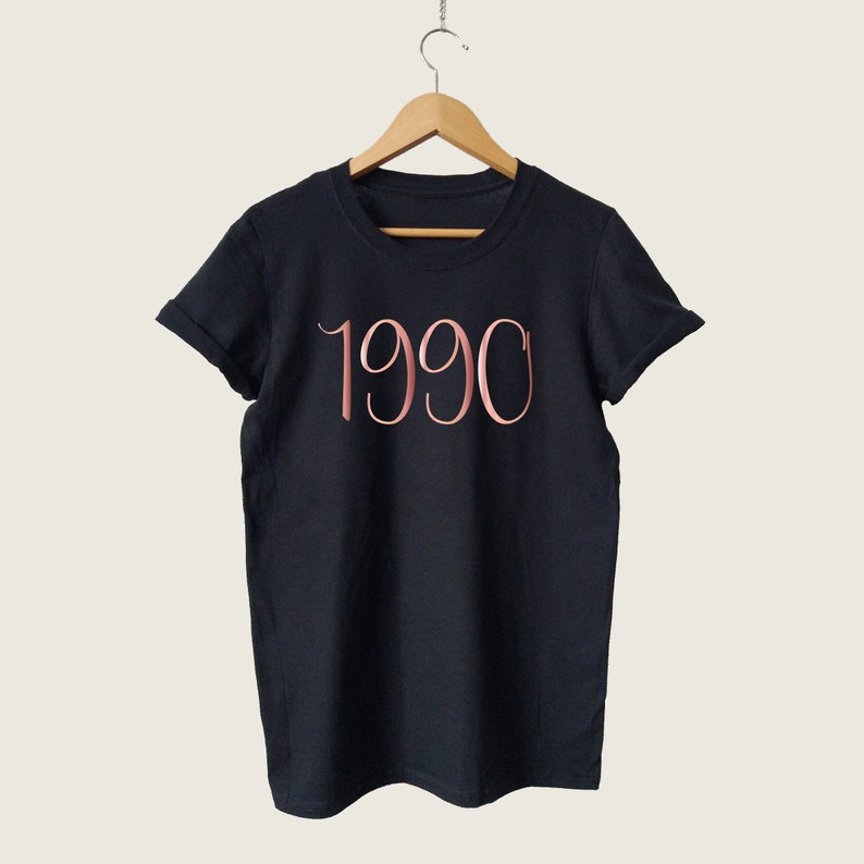 May include: Black t-shirt with a rose gold 1990 graphic.
