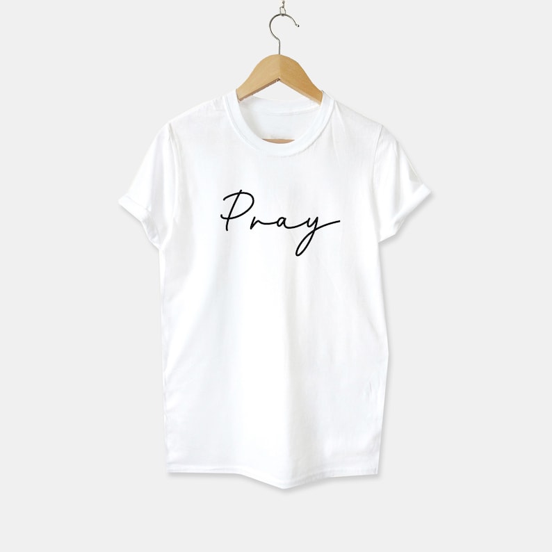 May include: White t-shirt with the word "Pray" written in black cursive script.