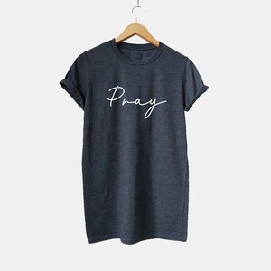 May include: A dark gray t-shirt with the word "Pray" written in white cursive script.