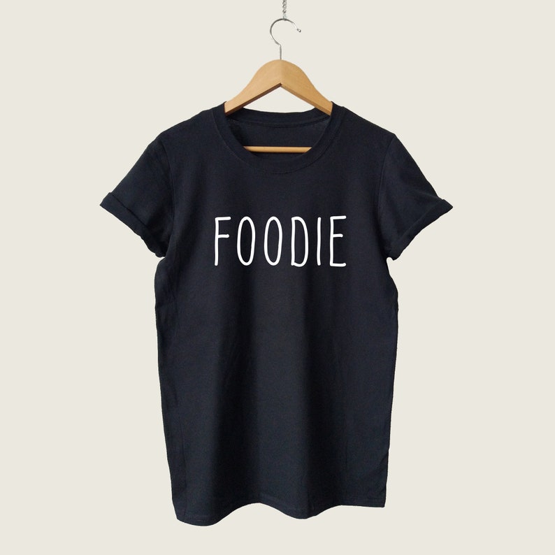 Puede incluir: Camiseta negra con texto blanco que dice "FOODIE" en la parte delantera.