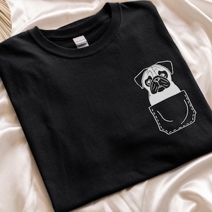Puede incluir: Camiseta negra con un gráfico blanco de un carlino asomándose de un bolsillo.