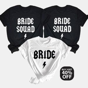 Peut inclure: Trois t-shirts noirs avec du texte blanc qui dit "Bride Squad" et un éclair. Un t-shirt blanc avec du texte noir qui dit "Bride" et un éclair. Achetez 3 et obtenez 40% de réduction.
