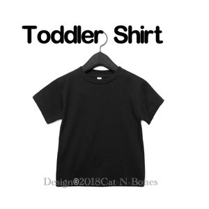 May include: Black toddler shirt hanging on a black hanger. The shirt is blank and has a crew neck. The text "Toddler Shirt" is above the shirt.